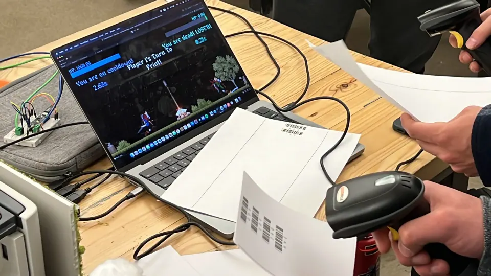 Playtesting Office Wizards: a laptop running the game, a barcode scanner in hand and printed barcode sheets on the table